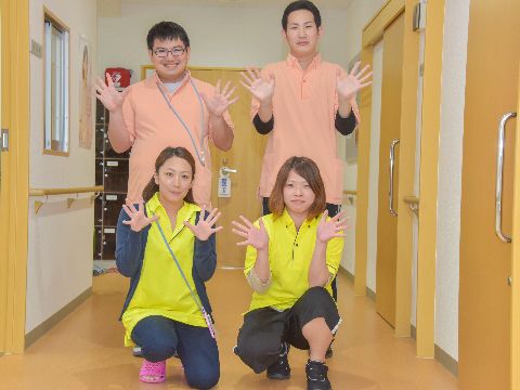 笑顔の女性スタッフ2名がしゃがんでおり、後ろには笑顔の男性スタッフ2名が立っている。みんな手を広げてポーズをとっている。