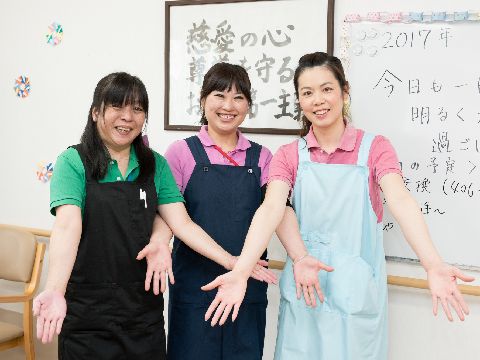 明るく元気な女性スタッフ3人が、両手を広げた同じポーズでホワイトボードの前に立っている。カラフルなポロシャツが印象的である。