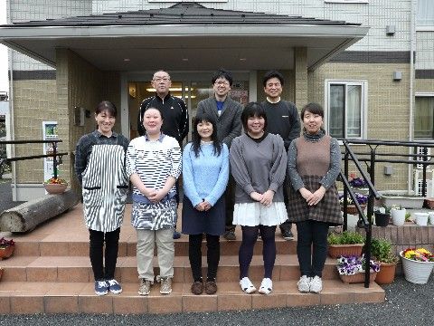 幅広い年齢層のスタッフ8名。前列は女性スタッフ、後列は男性スタッフ。入居者のグループホームでの生活のサポートをする。