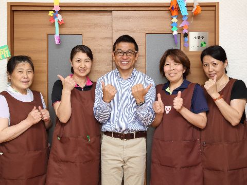 5人の職員たちが笑顔でポーズしながら相談室の前に立っている。折り紙で作られた七夕の飾りが飾られている。