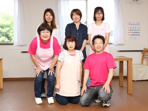 窓の前に施設の職員が六名、二列になってカメラのほうを向いて並んでいる。窓にはレースのカーテンが取り付けてある。