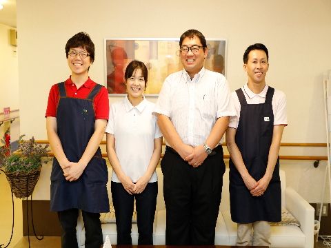 男女のスタッフの笑顔がある。ポロシャツとパンツで動きやすい服装である。エプロンをかけている男性もいる。