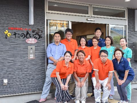 スタッフが11人、玄関前に並んでいる。制服はオレンジ色、紺色、薄緑色の3色があり、それぞれの役割が決まっている。