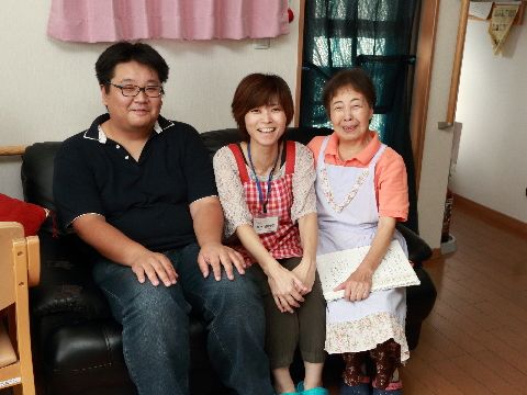 体格の良い男性スタッフと女性スタッフ2人が、黒いソファに笑顔で座っている。廊下には赤い消火器が置かれている。