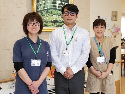 スタッフが３人横並びに立っている。男性がに中央に1人おり、両側に女性が２人いる。首からネームプレートを下げている。