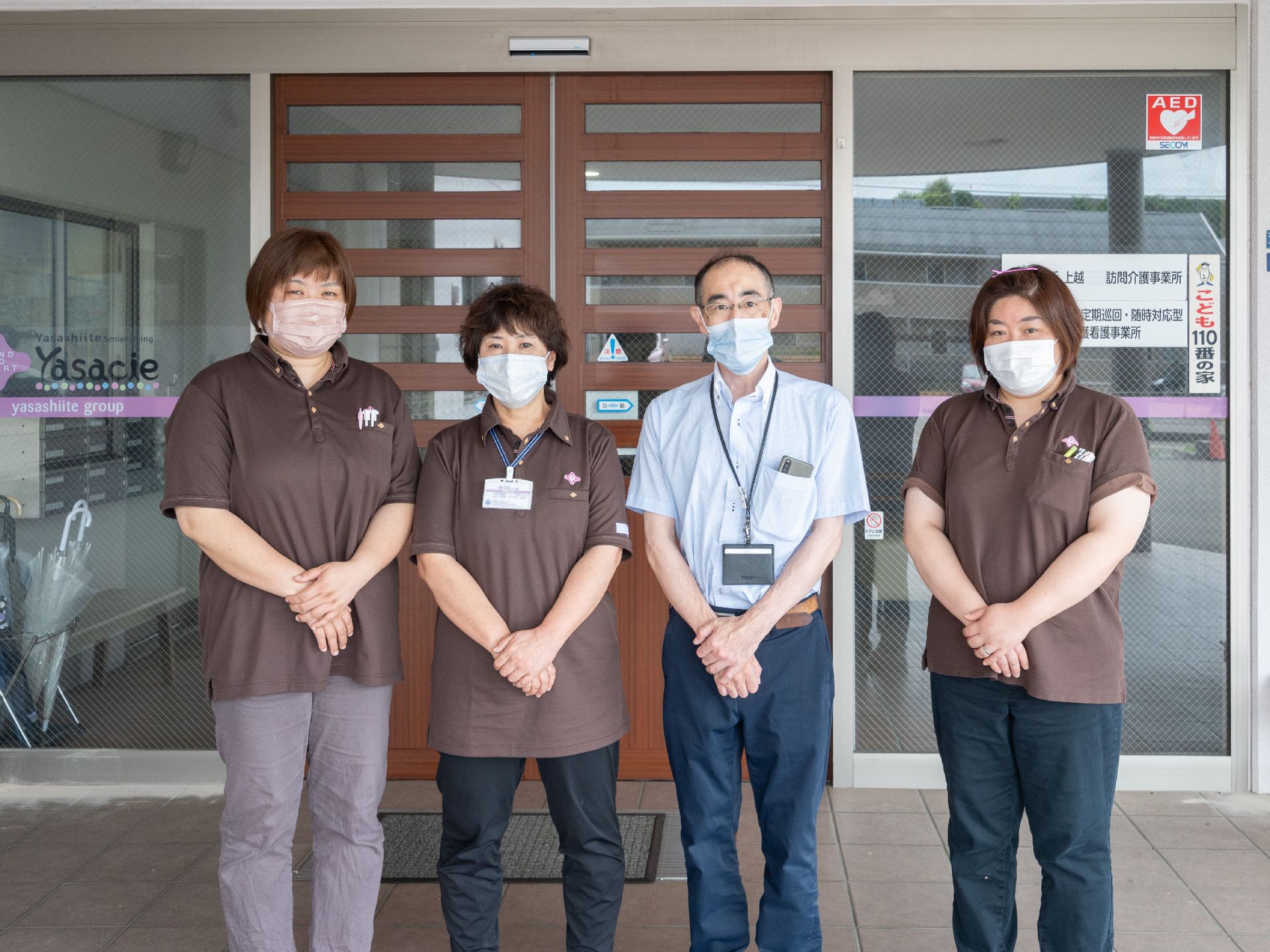 建物の入り口前に手を組んで並んでいる４人の従業員