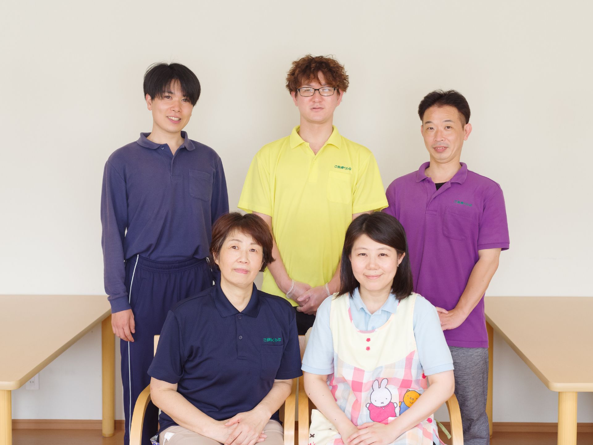 白い壁の前に並んでいる５人の従業員