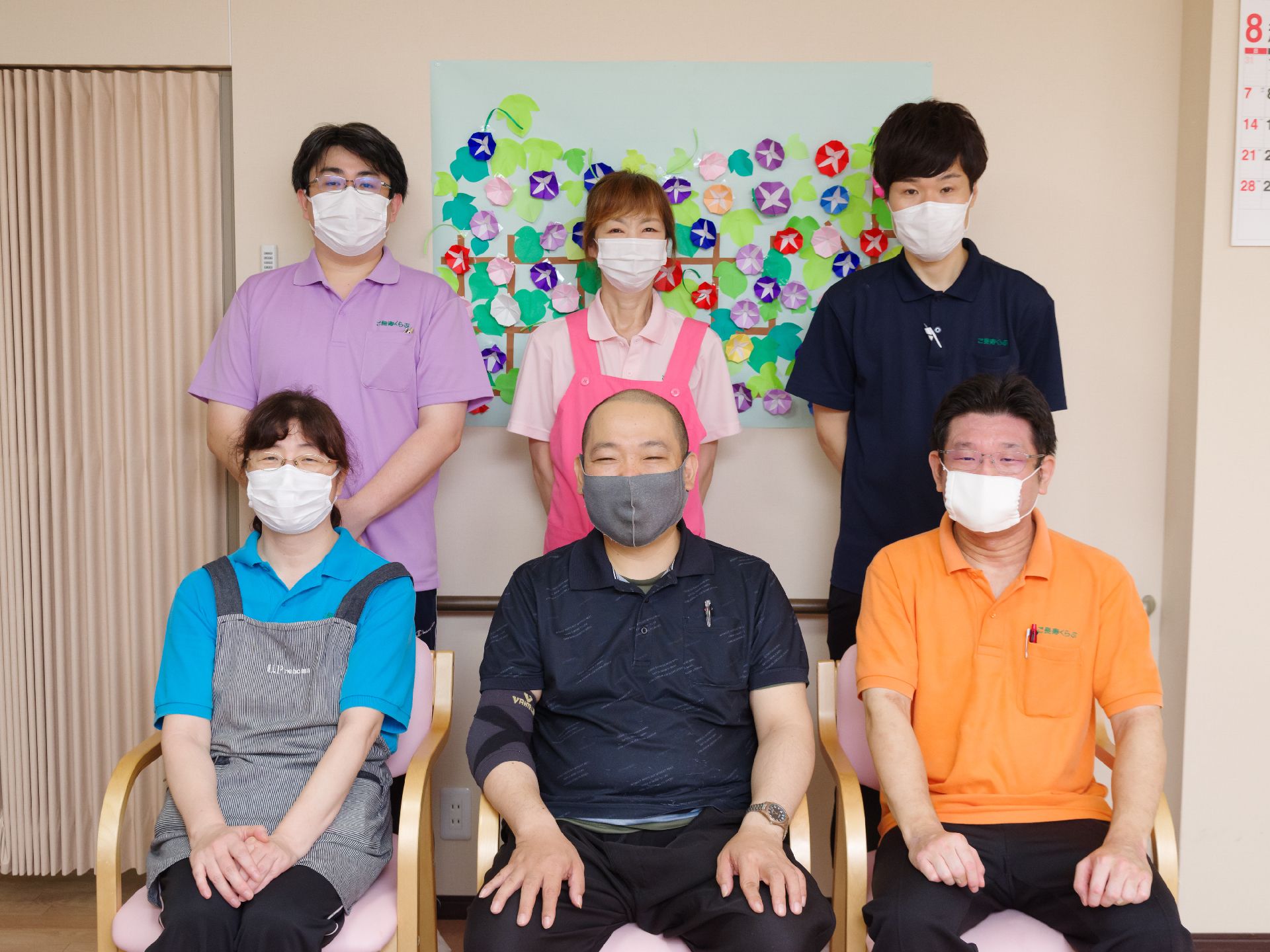 白い壁の前に並んでいる6名の従業員