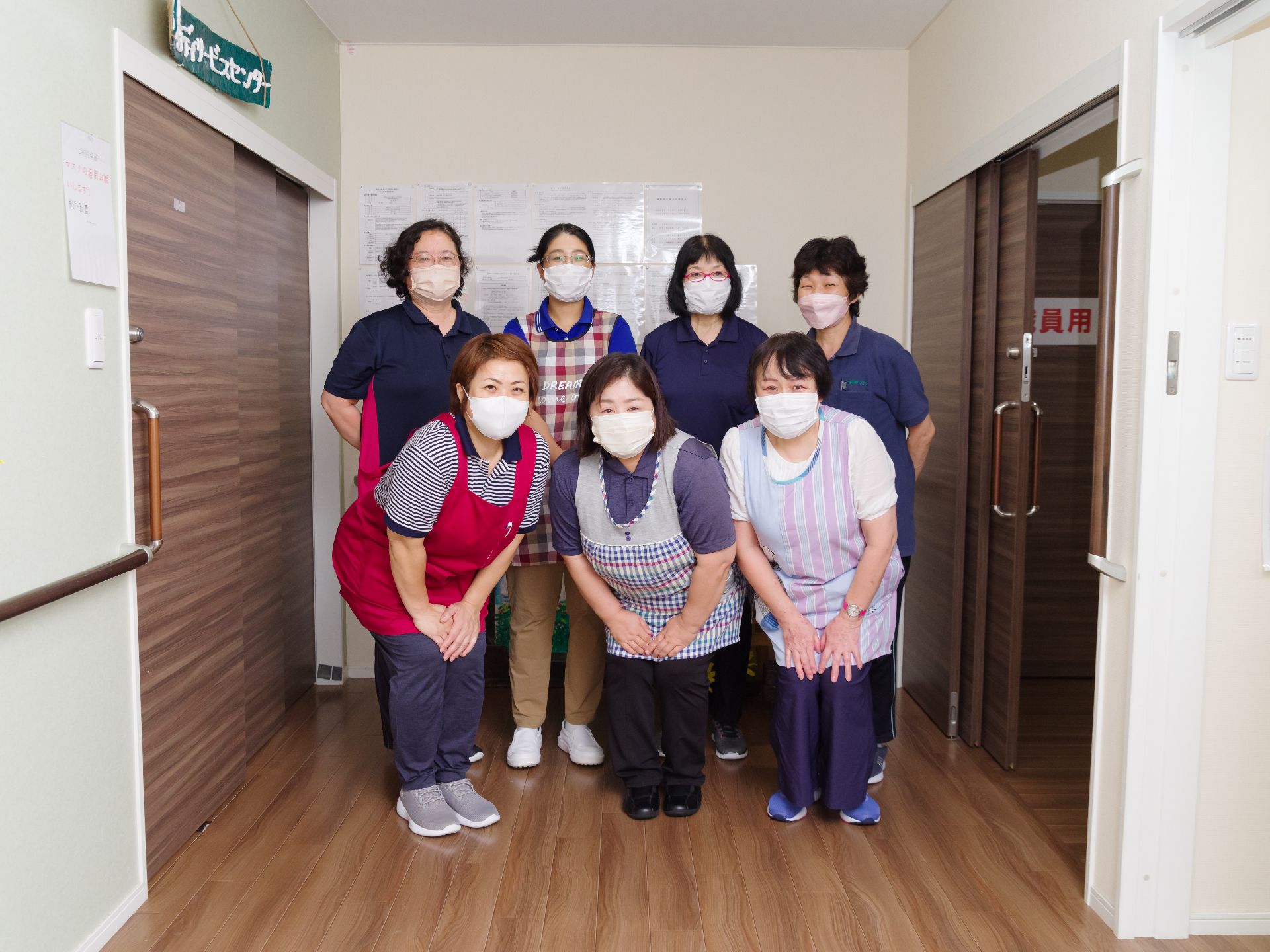 白い壁の前に並んでいる７名の女性従業員