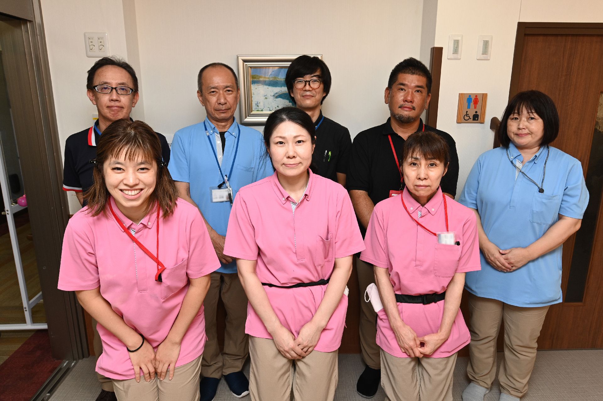 白い壁の前に立って２列で並んでいる８名の従業員