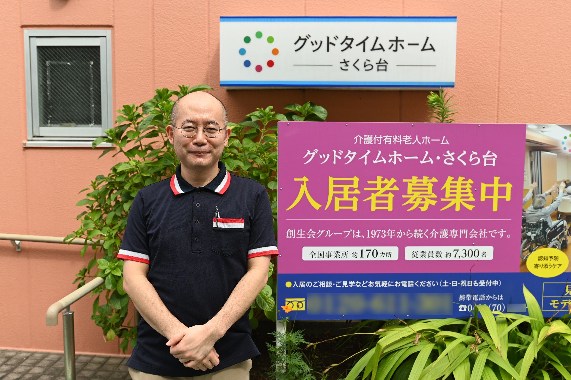 オレンジの外観の前のピンクの看板の横に立っている男性従業員