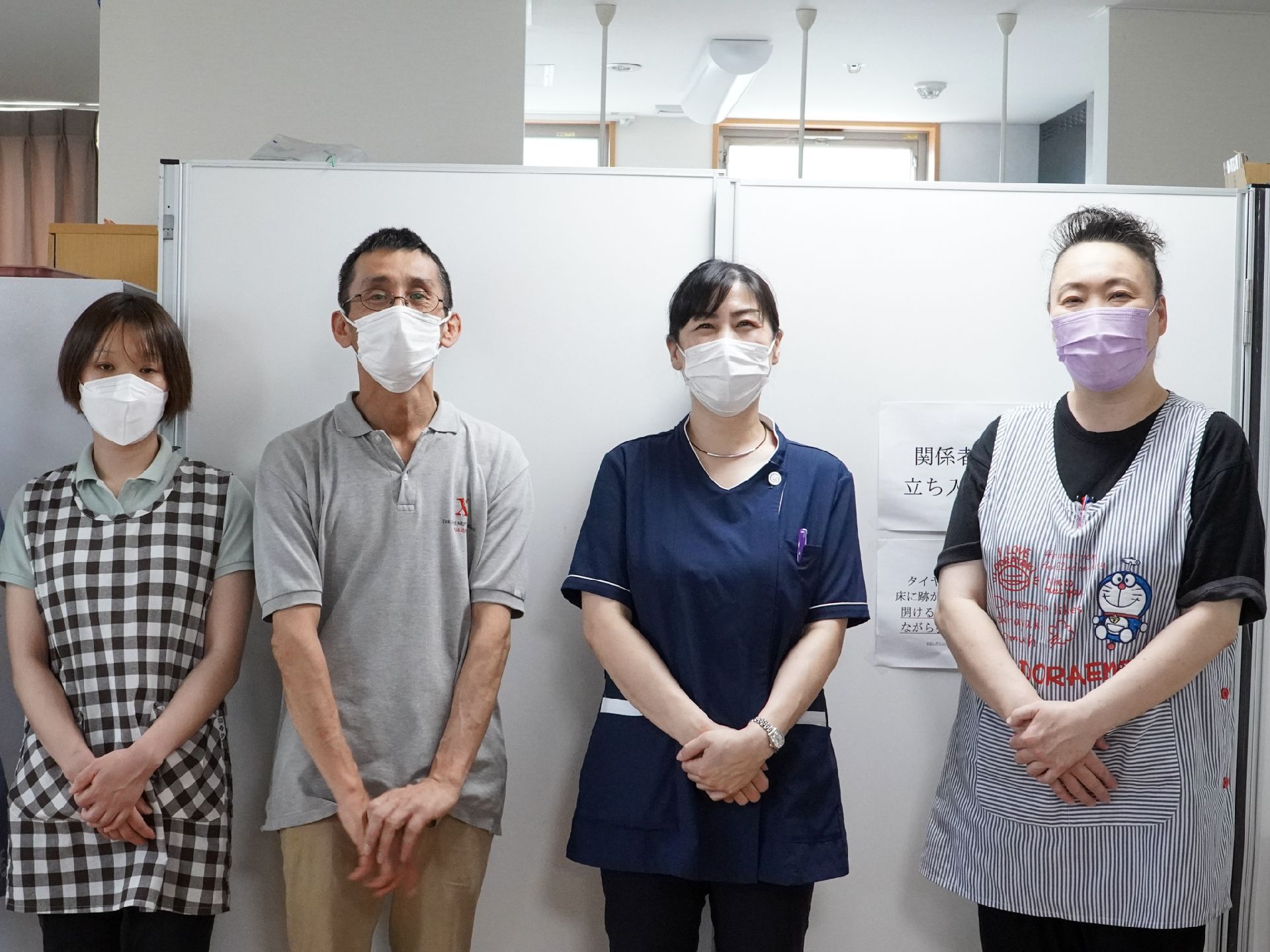 ホワイトボードの前に並んで立っている４名の従業員