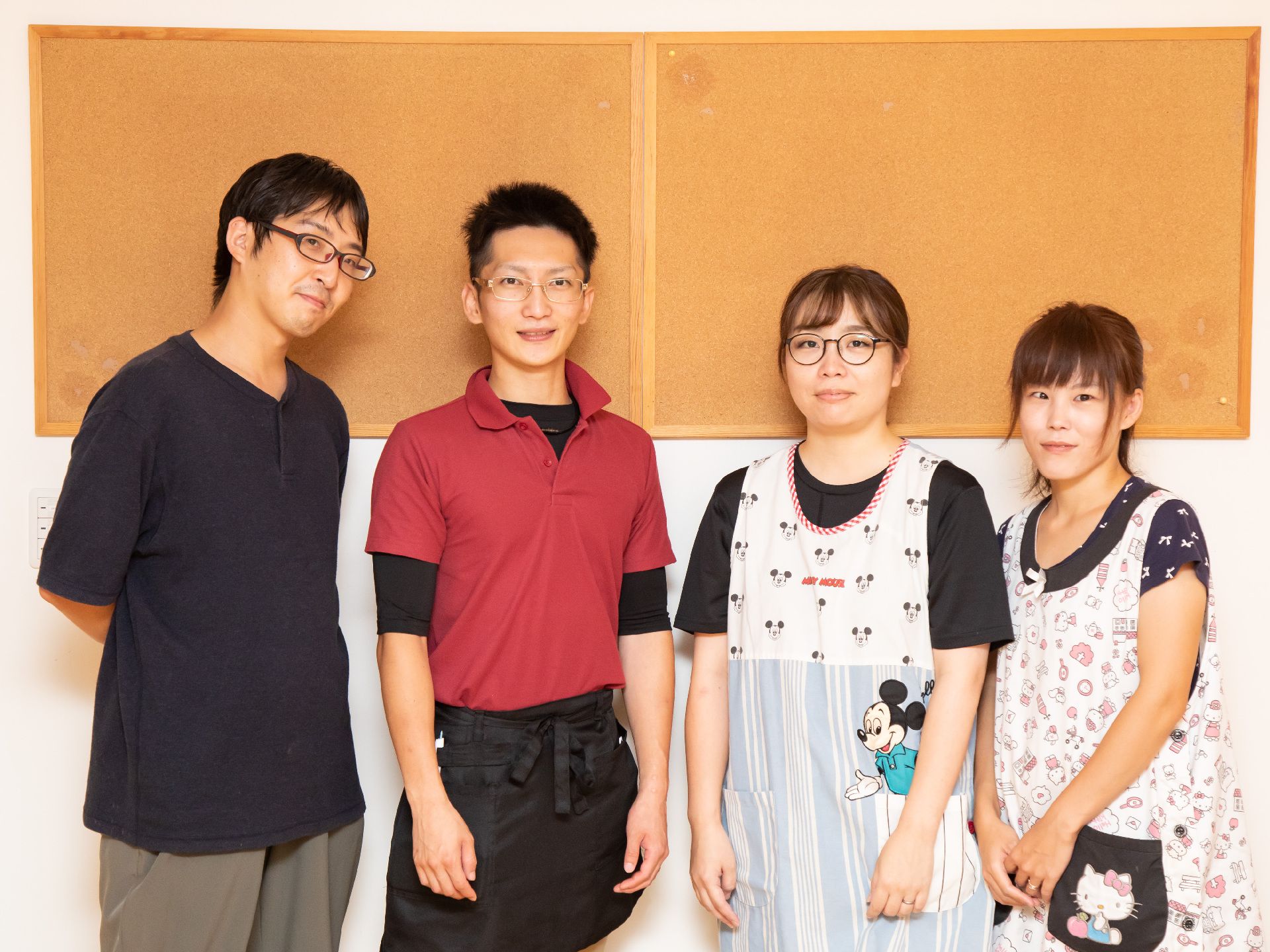 白と茶色の壁の前に並んで立っている４名の従業員