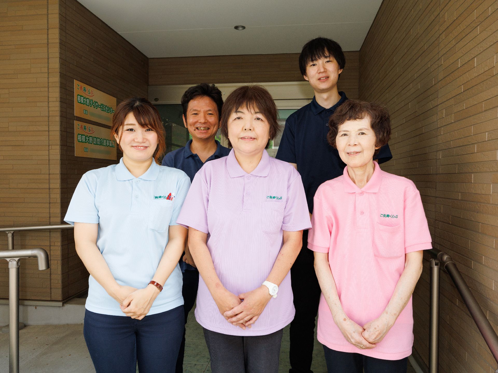 建物の入り口前に立っている５名の従業員