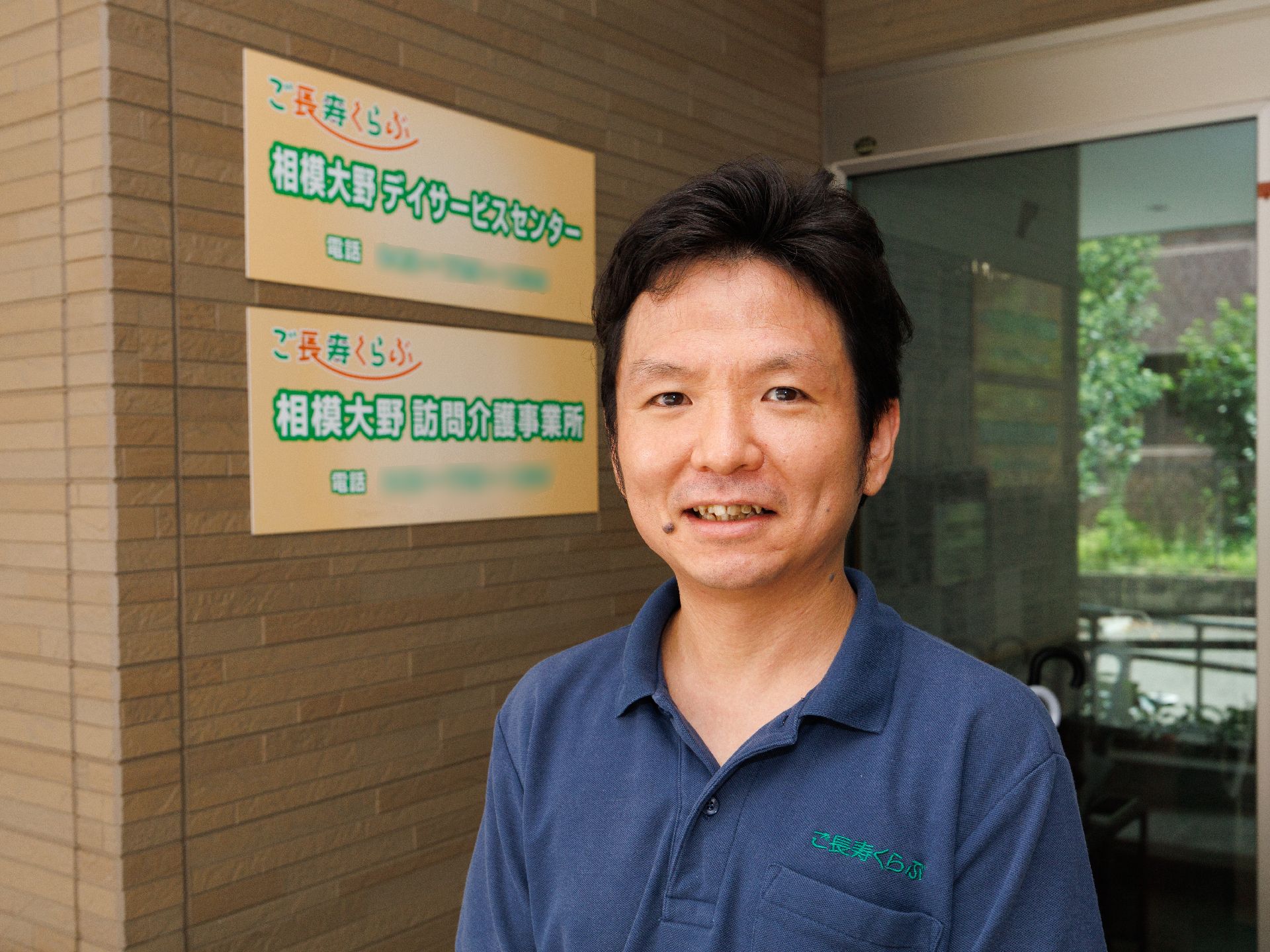レンガ調の壁の建物の入り口前に立っている男性従業員