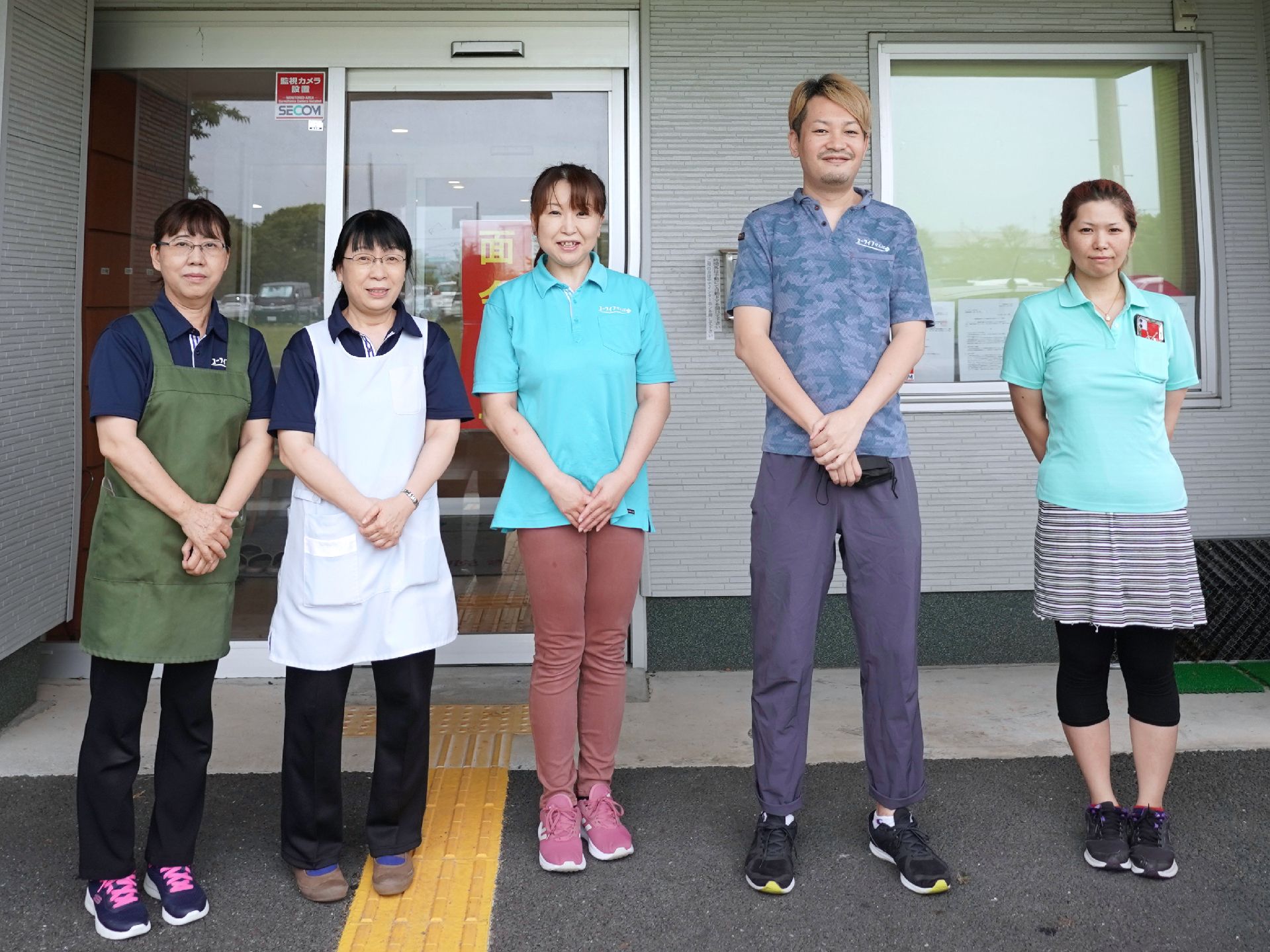建物の入り口の前に立って並んでいる５名の従業員