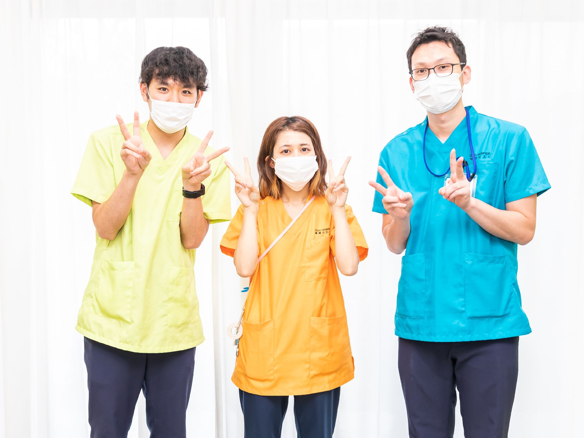 白いカーテンの前に並んで立っている３名の従業員