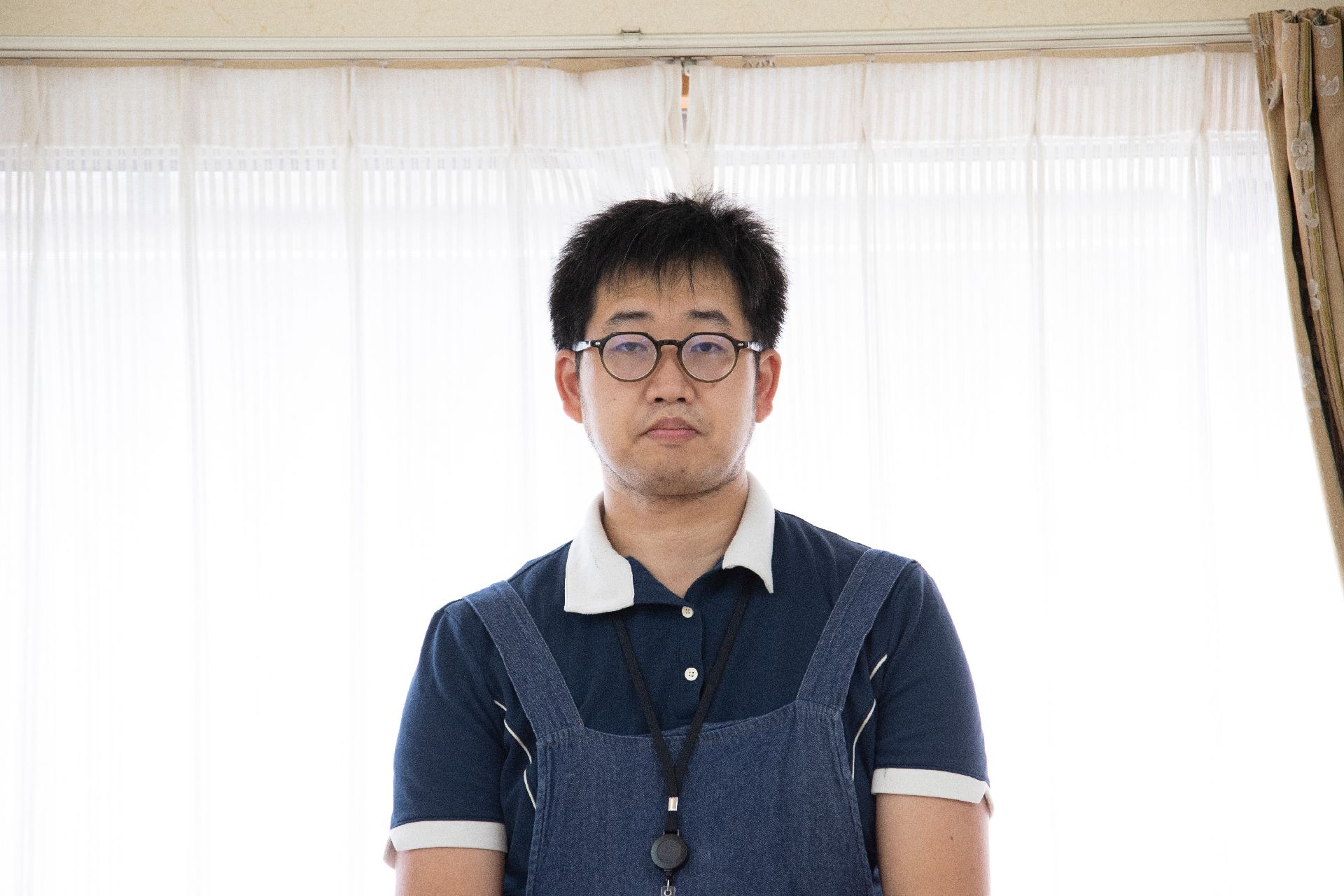 白いカーテンの前に立っているエプロンを付けた男性従業員