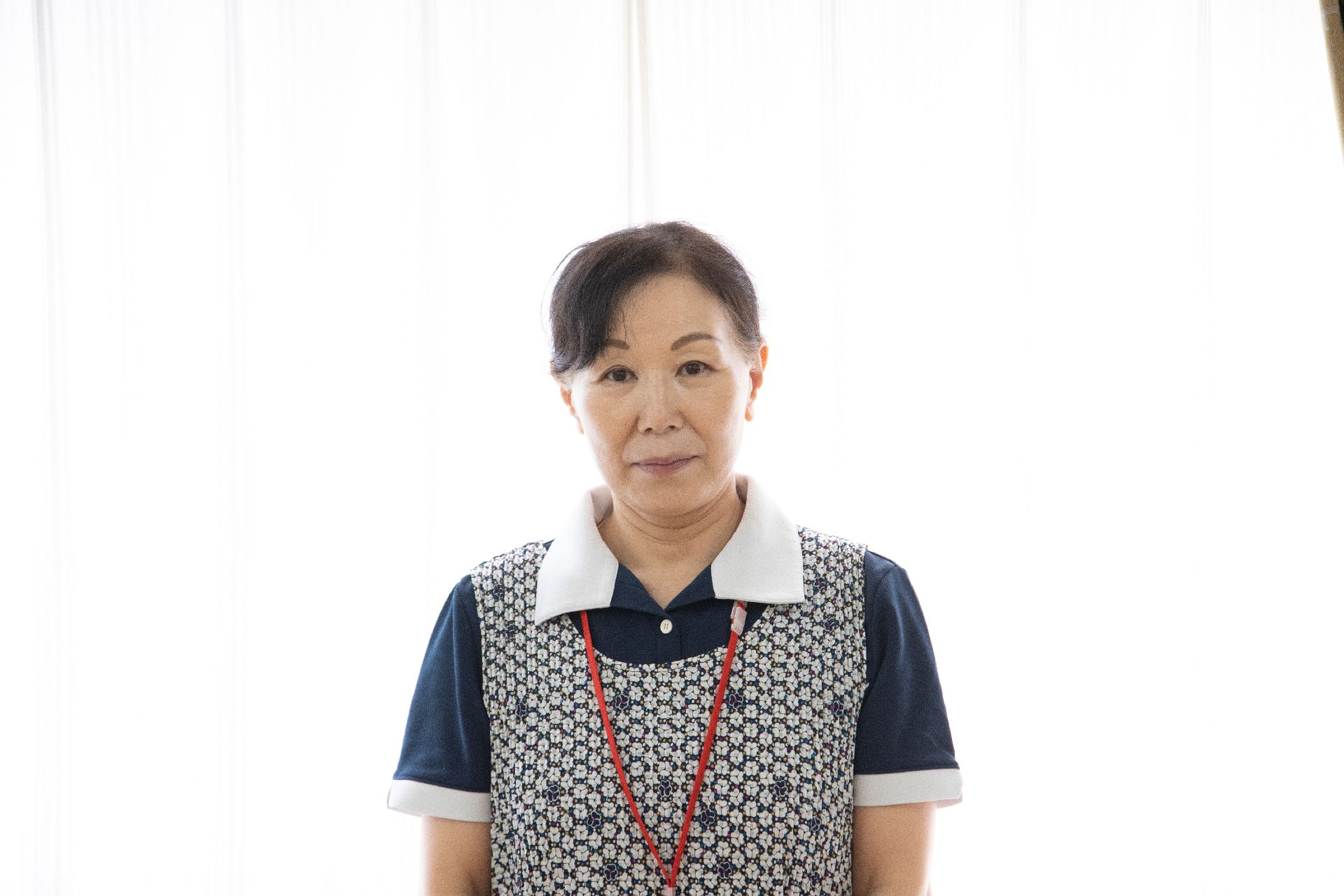 白いカーテンの前に立っている縞模様のエプロンを付けた女性従業員