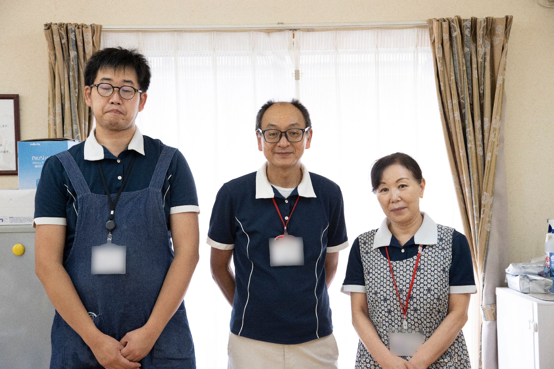 白いカーテンの前に並んで立っている３名の従業員