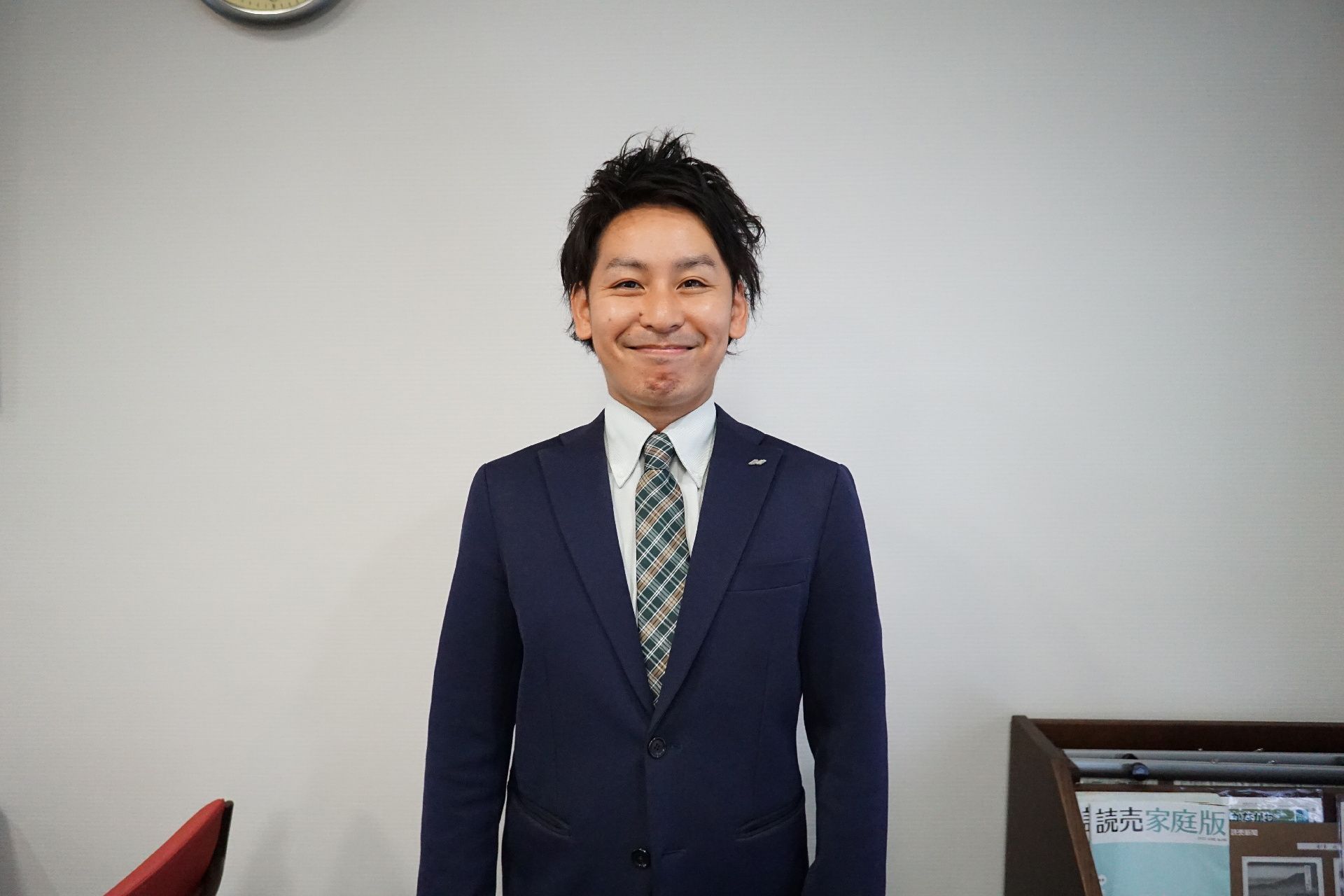 白い壁の前に笑顔で立っているスーツを着た男性