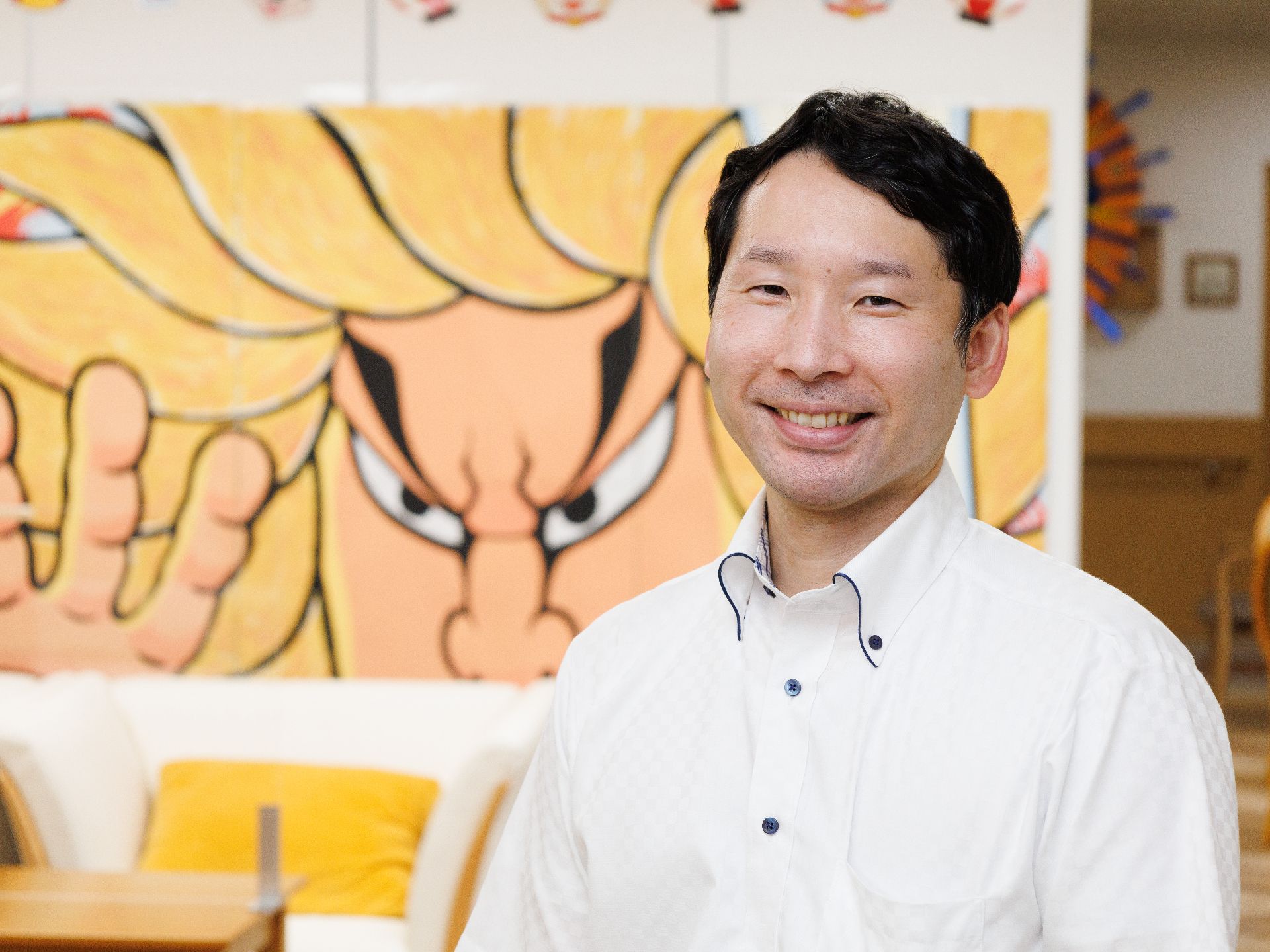 傾奇者が描かれた白い壁の前に立っている白いシャツを着た男性従業員