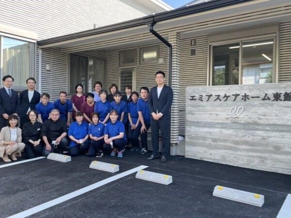 ブルーのポロシャツを着た男女のスタッフやスーツ姿の男性たちがホームの玄関周りに集まっている。