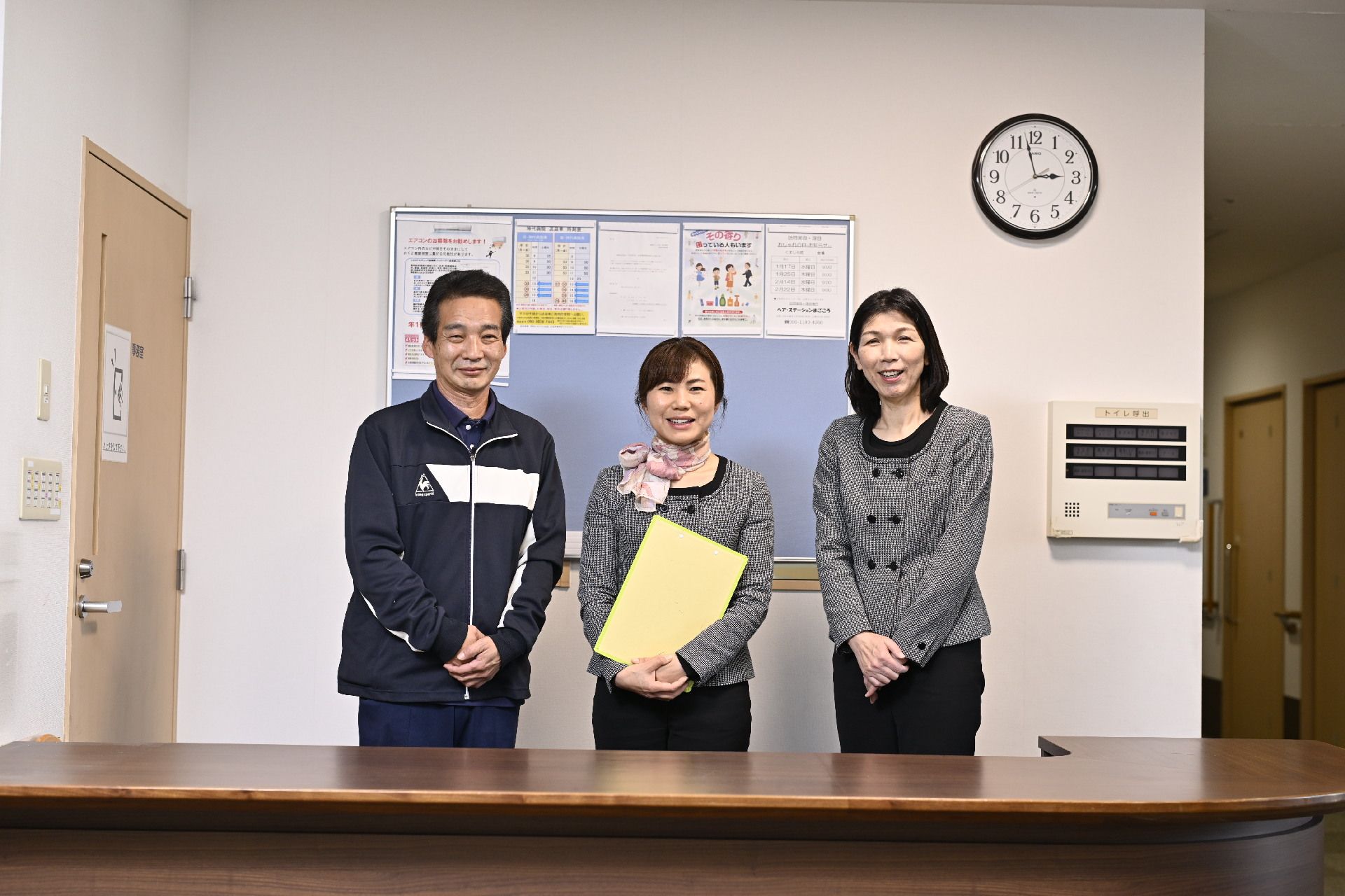 施設で働くスタッフの集合写真である。男性が4人と女性が6人、笑顔や柔らかい表情を見せている。テーブルに花が飾られている。
