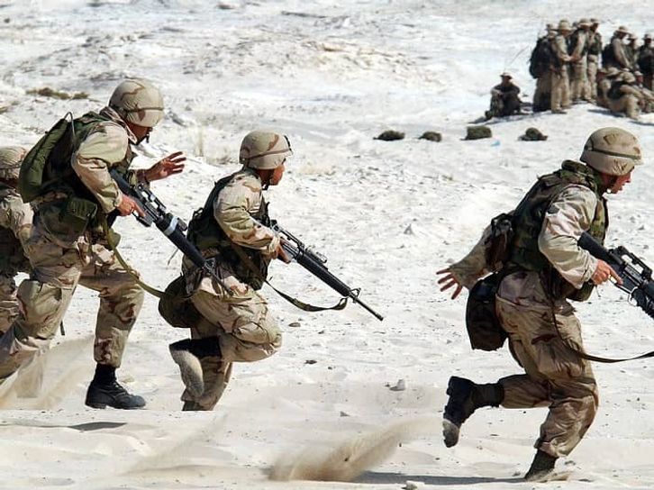 軍隊の兵士が機関銃を持って砂浜の上を走っている画像