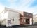 白を基調とした2階建ての建物の玄関部分はブラウンで、ベンチや自動販売機が玄関の周りに置かれ、青い空が広がっている。