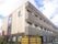 3階建ての建物はブラウン系の建物はベランダ付きで日当たりのいい場所にある。建物の周りには木が植えられ、窓もたくさんある。