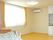 エアコンが設置された広いフローリングの部屋にはキッチンが付き、寝具がセットされたベッドが置かれ、窓にはレースカーテンとカーテンが付いている。