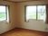 レースカーテンとカーテンが付いた窓が２つあるフローリングの部屋からは緑あふれる風景を見ることができる。