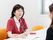 女性スタッフがペンを持ち、メモを取りながら笑顔で髪の長い女性の話を聞いている。