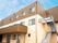 ブラウンとベージュの２階建ての建物は玄関に屋根があり、屋外階段が設置されている。