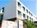 3階建ての建物は1階部分がブラウン、2階より上が白で、周辺には緑も多い。