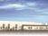 ベージュの外壁の建物は日当たりのいい場所にあり、駐車場もある。数名の人が玄関の周りにいある。