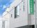 白い建物の1階部分は駐車スペースとなっていて、外壁には緑の看板がかかっている。
