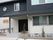 2階建ての建物はモノトーンで和モダンの雰囲気。玄関には屋根が付き、手すり付きのスロープや階段もある。