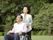 公園を散歩している高齢者夫婦。車いすに乗っている人とそれを押す人がほほ笑んでいる
