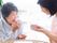 薬を飲もうとしている高齢女性と付き添いのコップを持って微笑んでいるエプロンを付けた女性スタッフ。