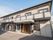 日当たりのいい場所に建っているベージュの外壁の2階建ての建物。玄関に屋根もある。