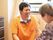 オレンジ色の服を着た男性が、高齢者と目線を合わせて会話をしている