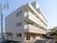 4階建ての建物は重厚感があり、白っぽい色でまとめられている。周辺には住宅があり、敷地内には点字ブロックが敷かれている。