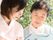 カルテのようなものを見ながら若い女性スタッフと話をしている高齢女性。二人とも真剣な表情。後ろには緑がたくさんある。