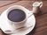 テーブルの上に置かれた白いカップにはコーヒーが入っていて、横にはミルクが添えられている