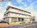 各フロアにベランダが付いた3階建ての建物は道路に面していて、駐車スペースもある。駐車スペースには車が一台止まっている。