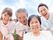 車いすの高齢女性と介助をしている高齢男性を囲み、若い男女のスタッフがいる。4人とも笑顔で屋外で過ごしている。