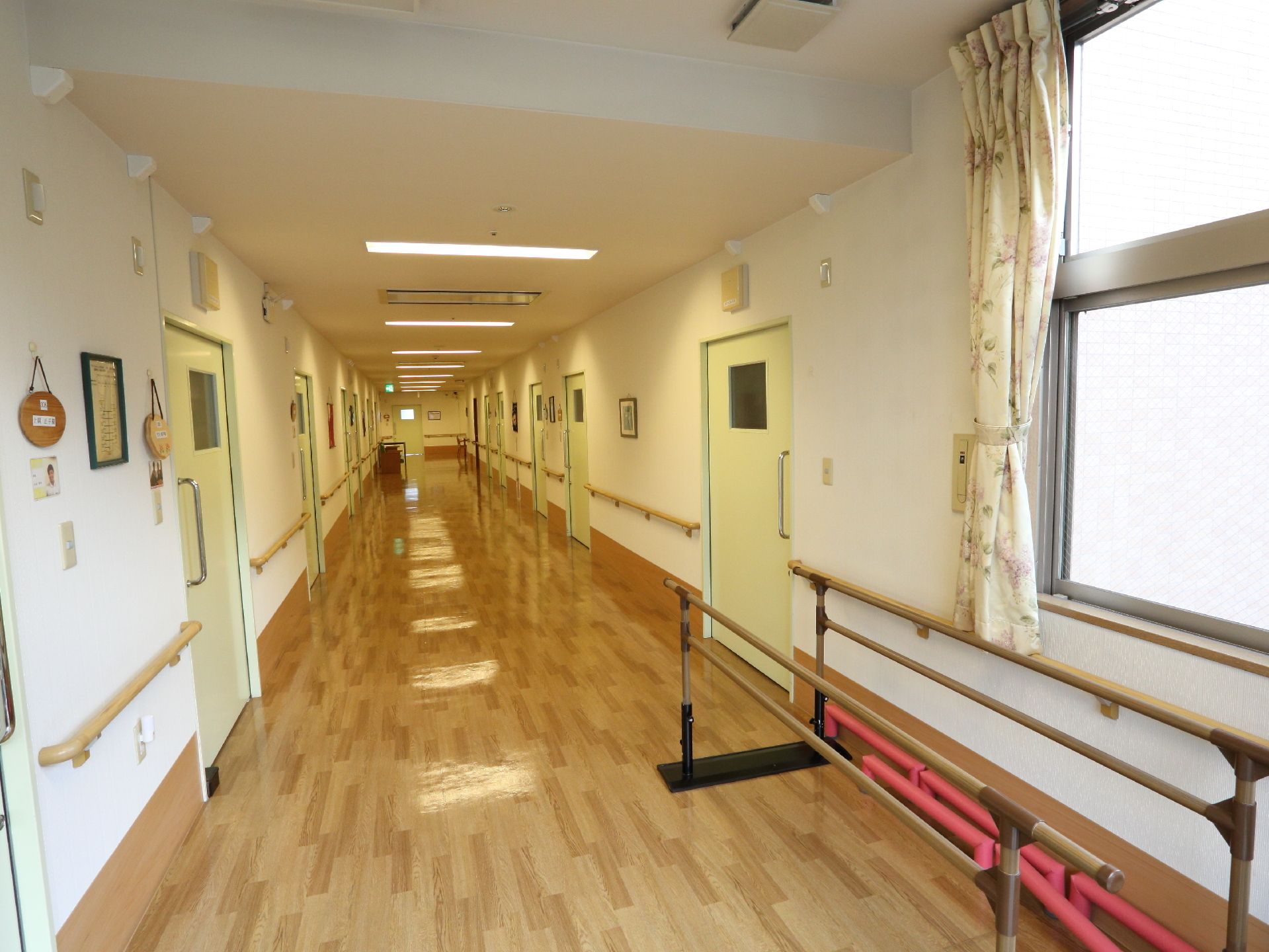 廊下の右側の手前に歩行練習用の手すりが設置されている。通路の両側には手すりがついている。窓も大きい。