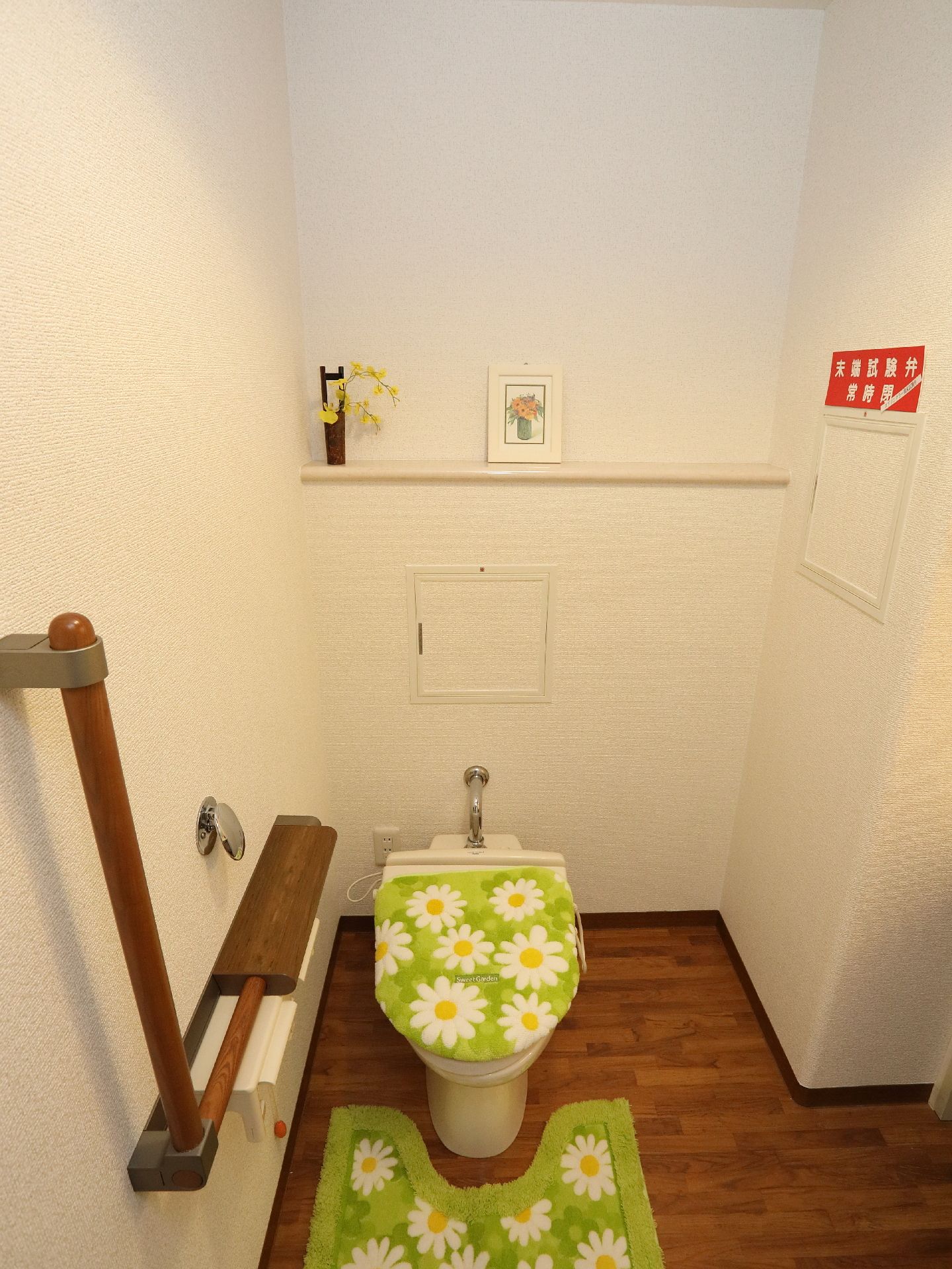 家庭的なトイレ。濃いめの木目フローリングの為、汚れが目立ちにくい。手すりもきちんとあり、配慮されている。